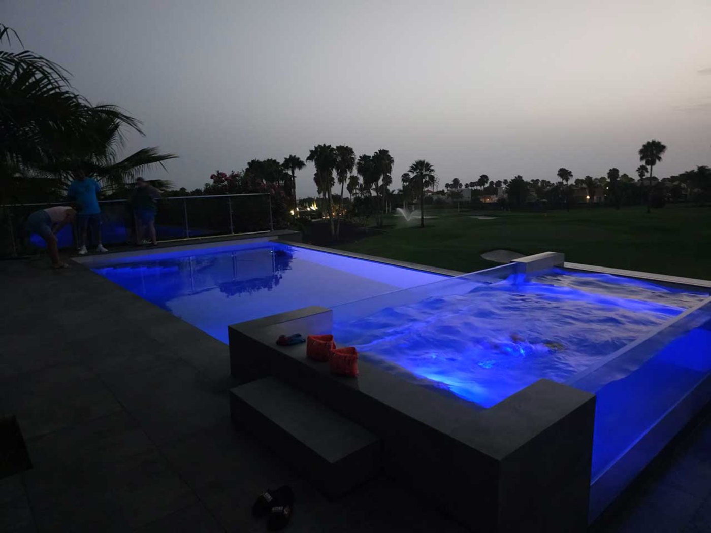 Piscina de hormigón iluminada al anochecer junto a un campo de golf, con el agua en movimiento